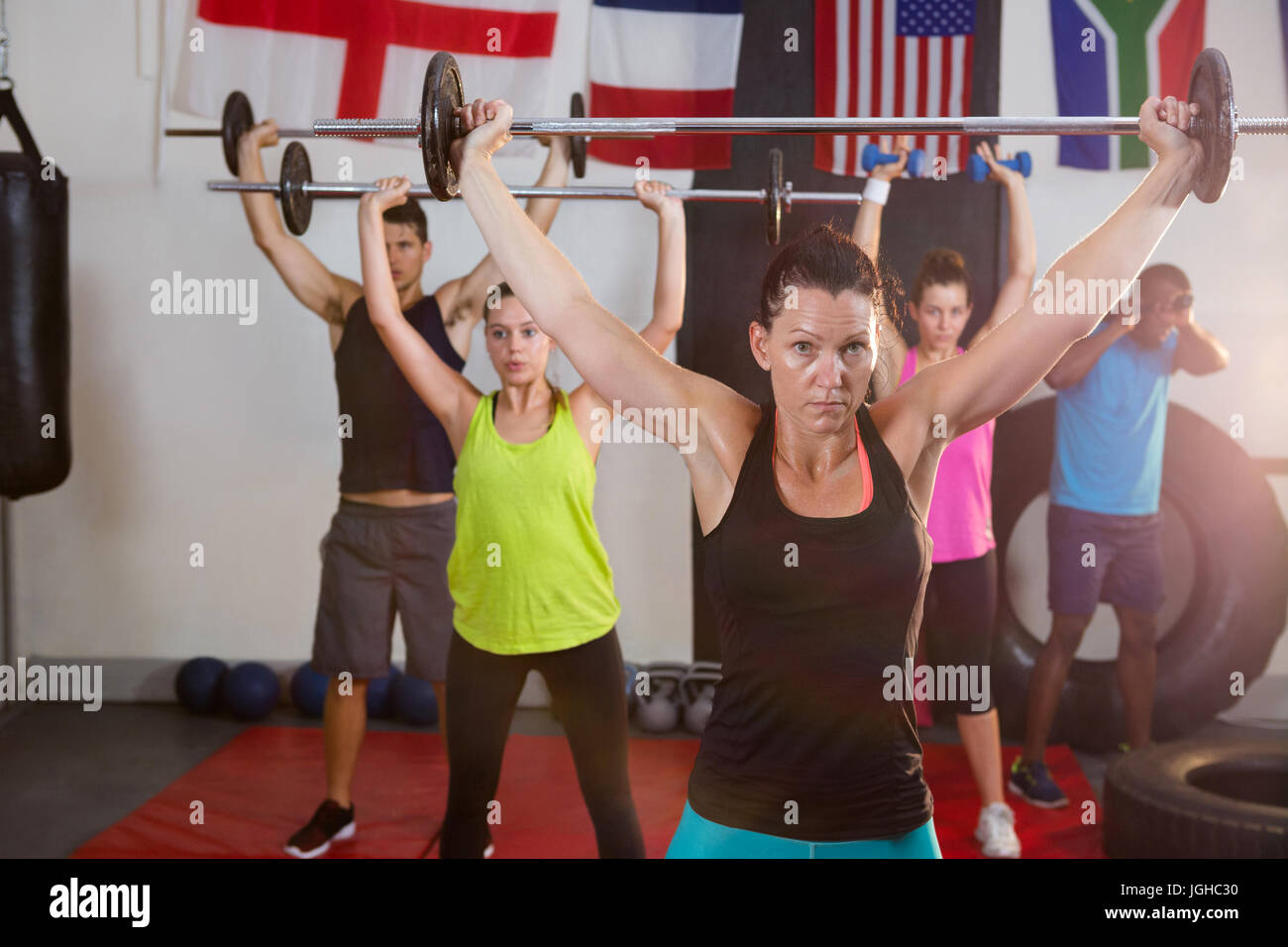 Young athletes lifting barbells against flags at fitness studio Stock