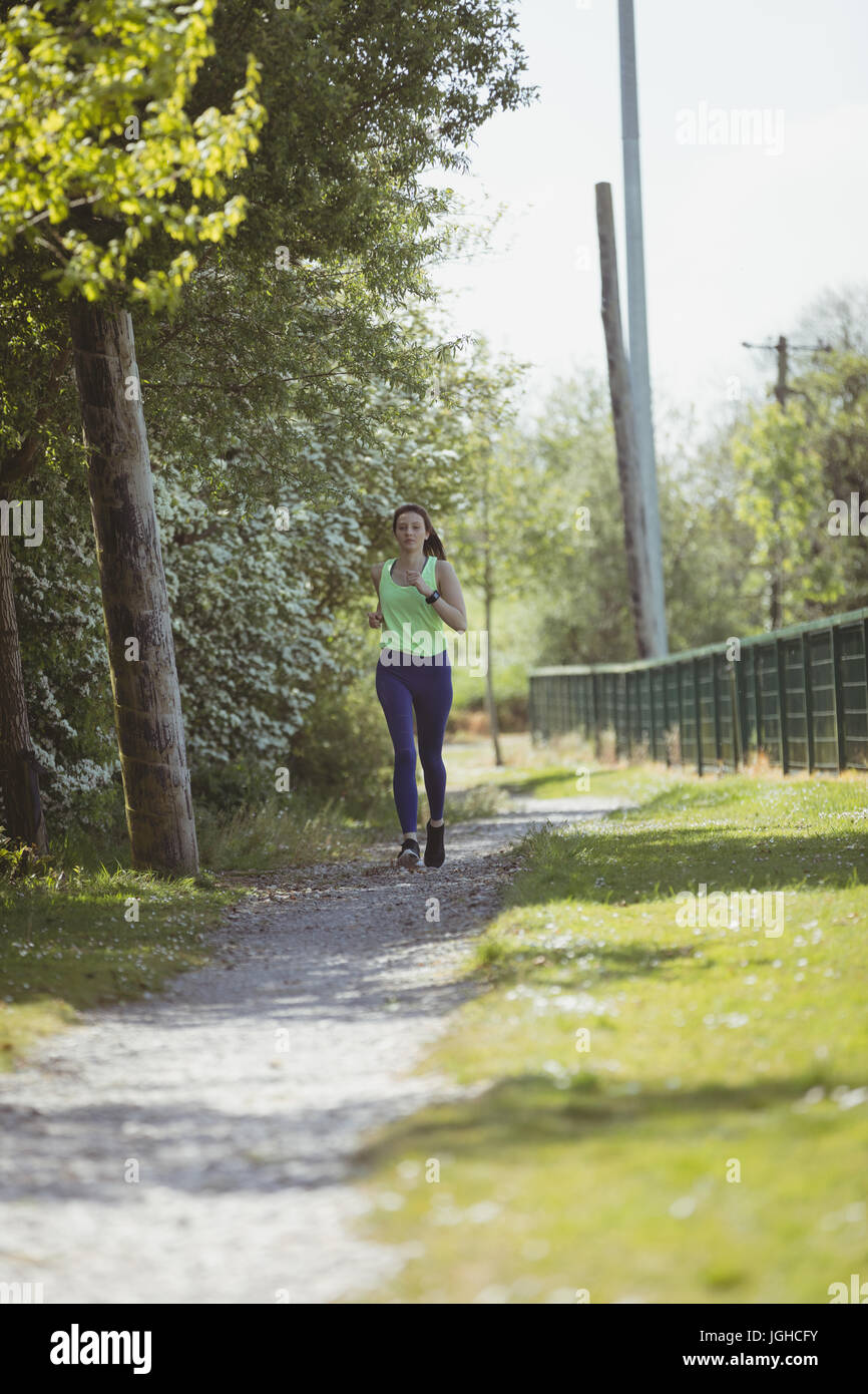 Full length of female athlete jogging by trees on pathway Stock Photo ...