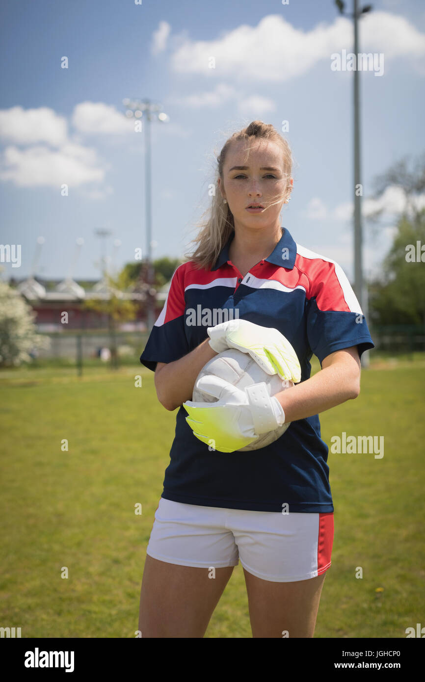 Portrait of female goalie with soccer ball standing on field against