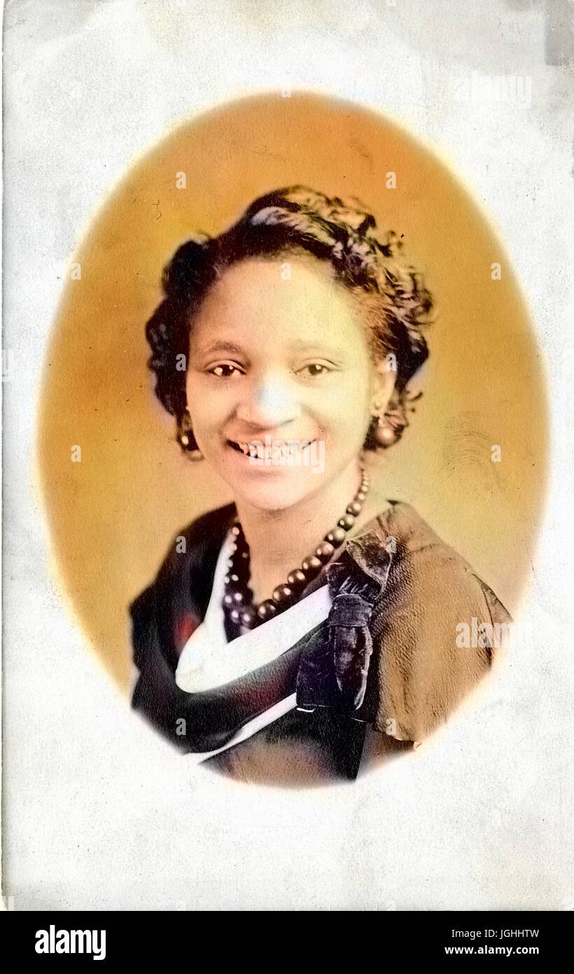 Headshot of young African American woman, wearing a necklace, earrings and a dark dress with a bow, smiling, 1920. Note: Image has been digitally colorized using a modern process. Colors may not be period-accurate. Stock Photo