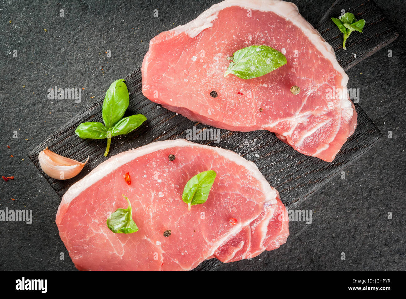 Raw organic meat. Pork steaks, fillets for grilling, baking or frying. On a wooden cutting board, with salt, pepper, basil, tomatoes, garlic. On a gra Stock Photo