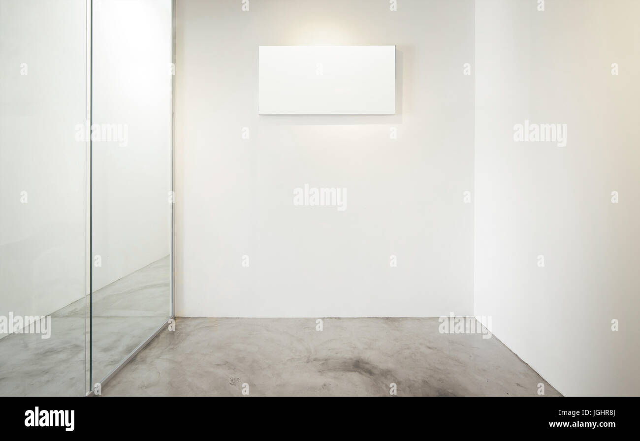 Empty office room, Glass window to the left .Loft interior style , white canvas print on the center white wall. concrete floor . Stock Photo