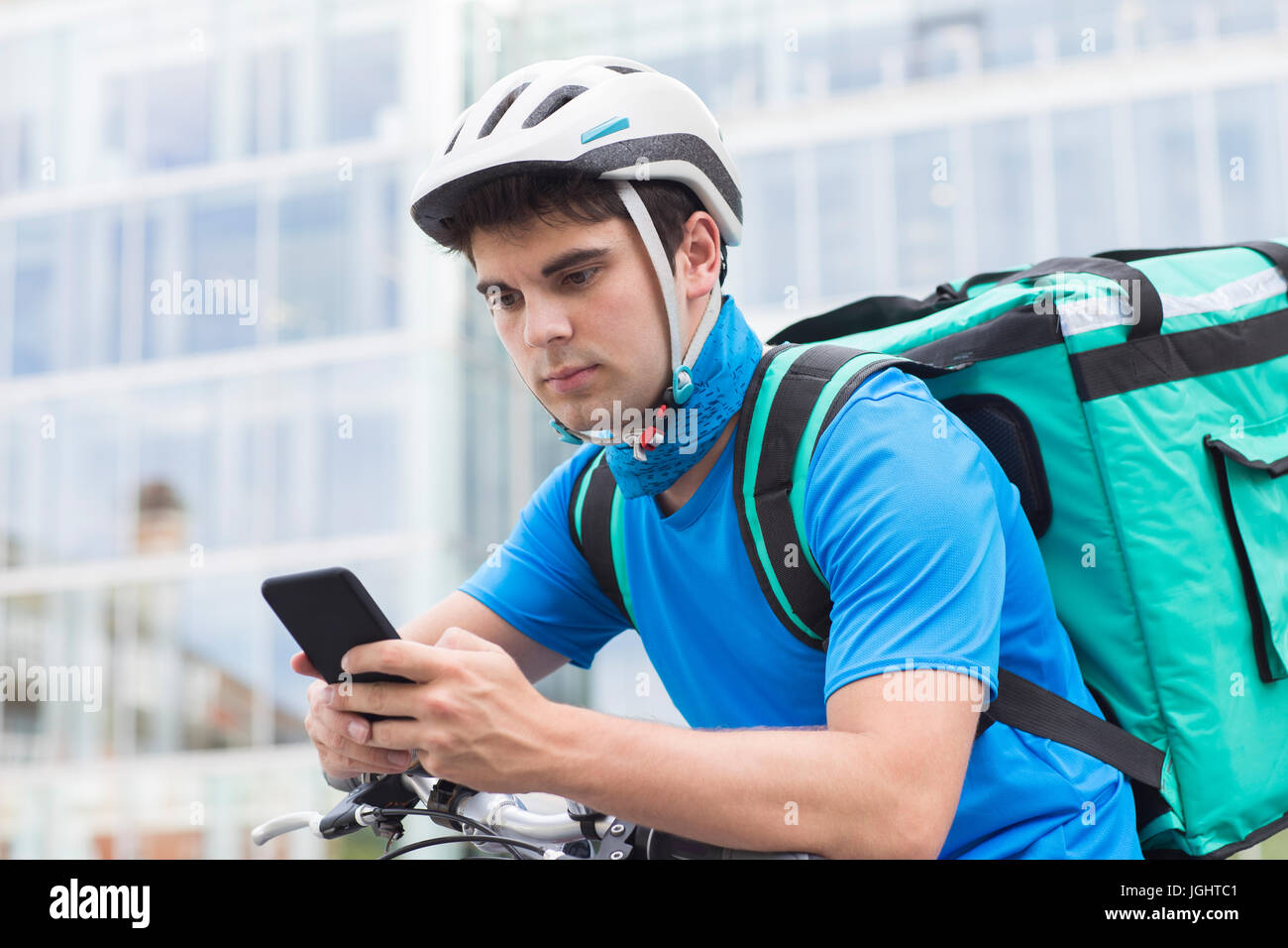 Courier On Bicycle Delivering Food In City Using Mobile Phone Stock Photo