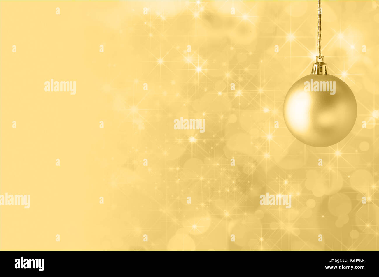 A golden yellow Christmas bauble, suspended on gold string against a star filled twinkly bokeh background, fading into solid colour to provide copy sp Stock Photo