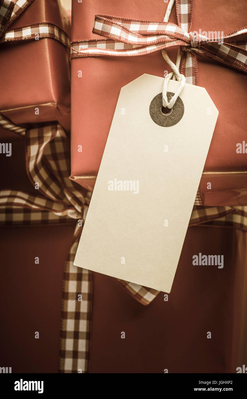 Close up of gift packages wrapped in red paper with gingham check ribbon, tied in bows, with traditional blank parcel tag on string facing upwards to  Stock Photo
