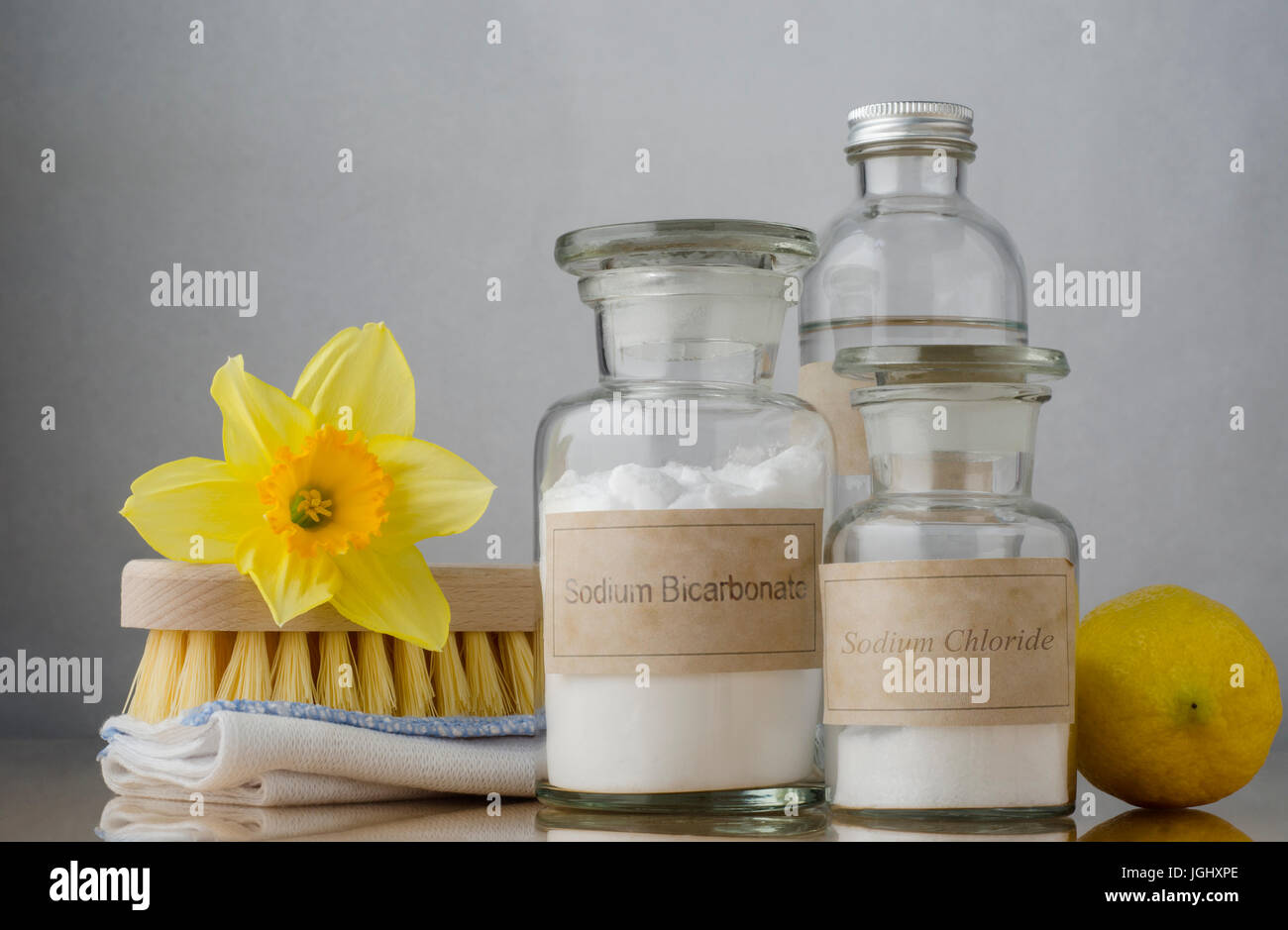 Still life of natural cleaning choices.  Sodium bicarbonate and salt in apothecary jars, white vinegar behind them and a lemon to the right.  A folded Stock Photo