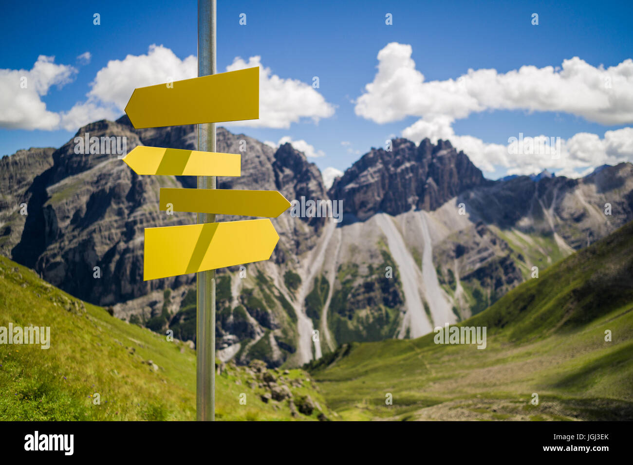 Blank hiking signs on a pole in front of a blurred landscape with mountains and blue sky Stock Photo