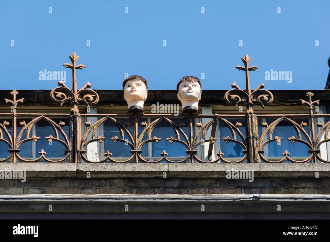 Two severed male mannequin heads impaled on railings on a metal fence Stock Photo