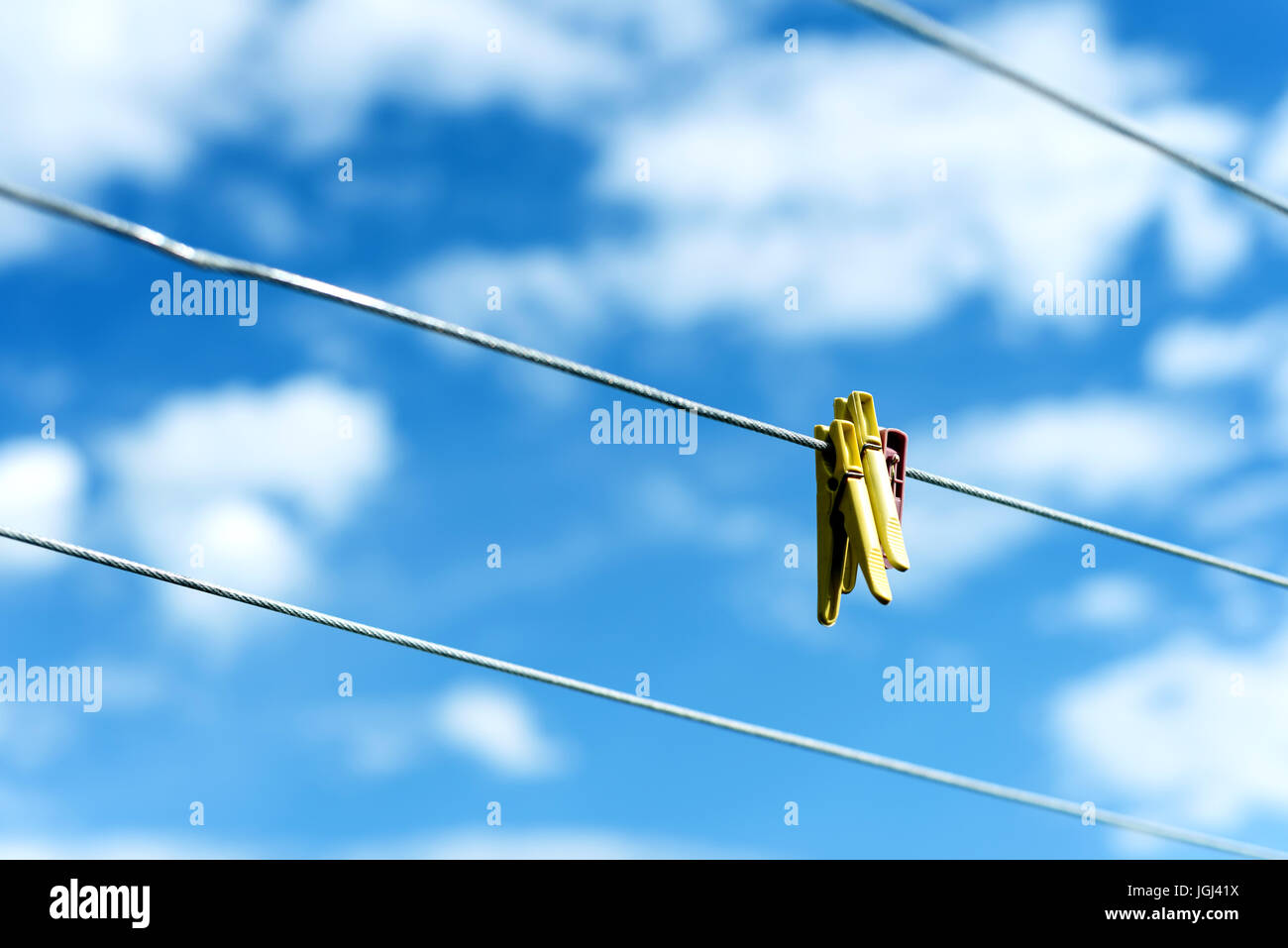 Three brightly colored plastic clothes pegs on a  family washing line with blue sky and white summer clouds in the background Stock Photo