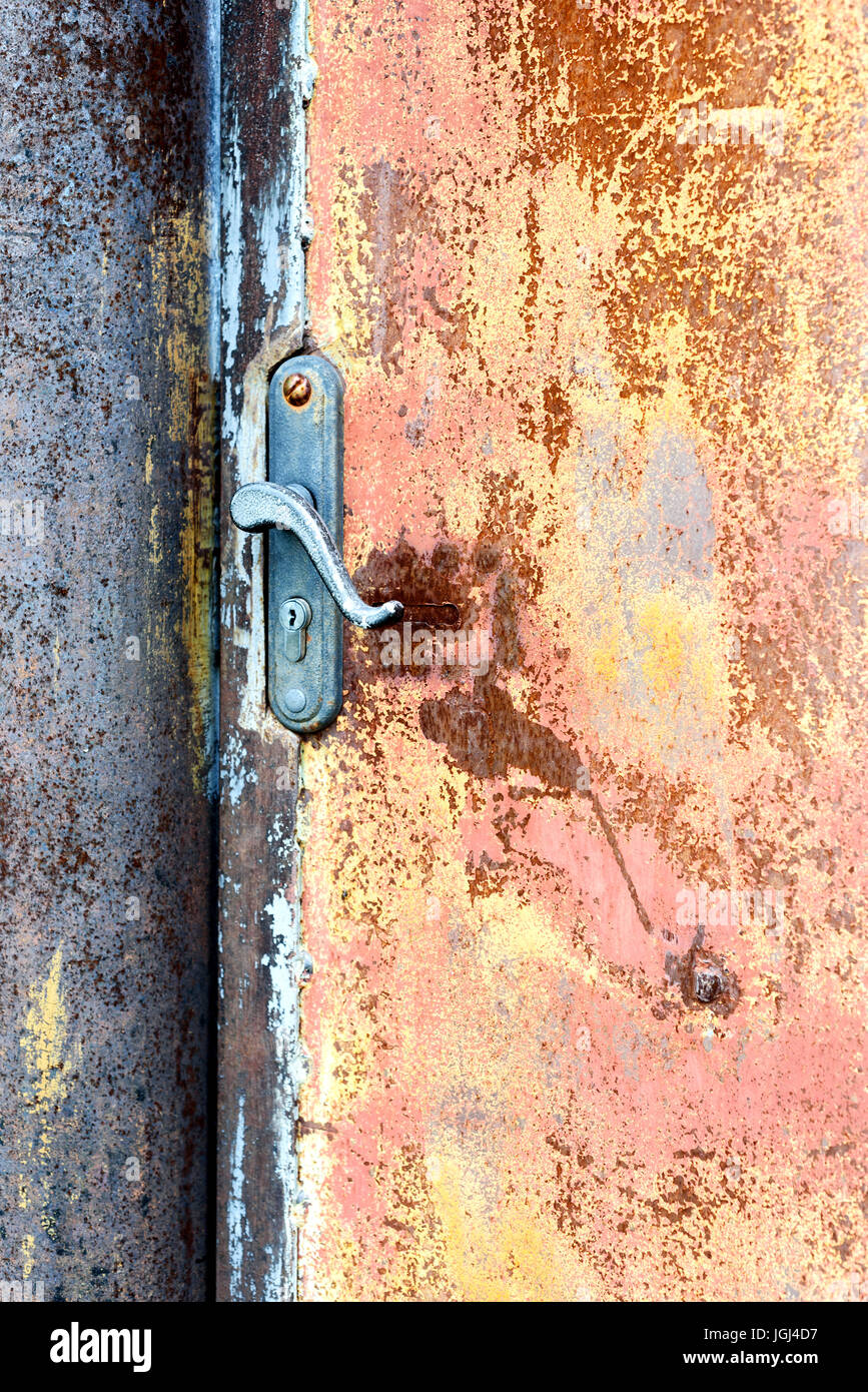Single locked rusty house door handle set against a deteriorating sheet metal covered in oxidized particles Stock Photo