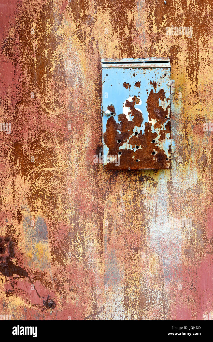 Rusty neglected vintage metal post box attached to a rust covered metal wall with deterioration Stock Photo