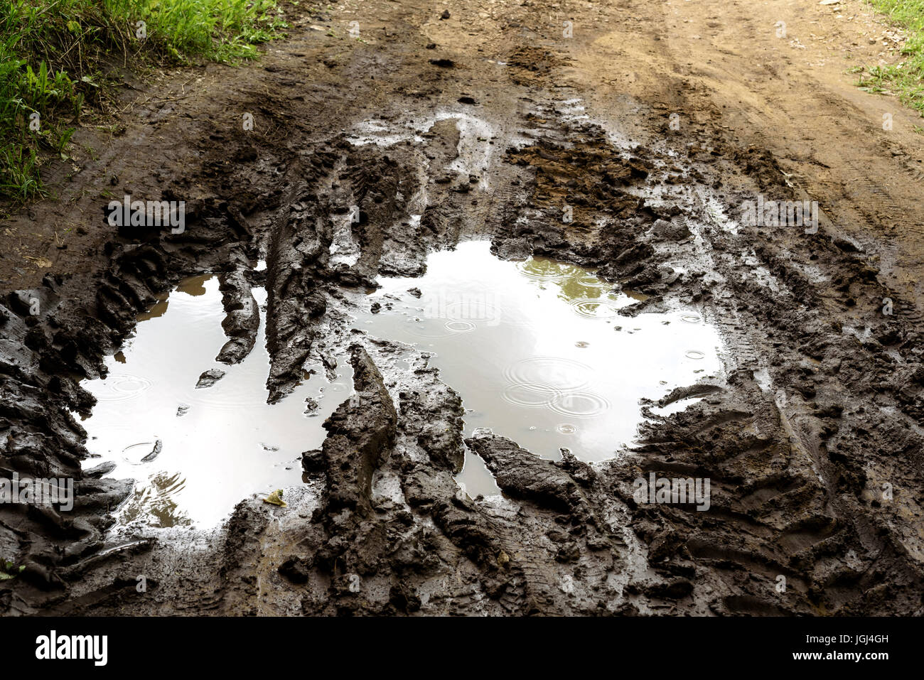 Rain filled muddy puddle with vehicle tracks on a dirt track road Stock Photo