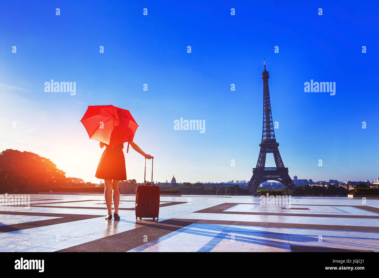 Pretty young woman with stylish red clothes, umbrella and suitcase near Eiffel Tower in Paris, France, capital of fashion Stock Photo