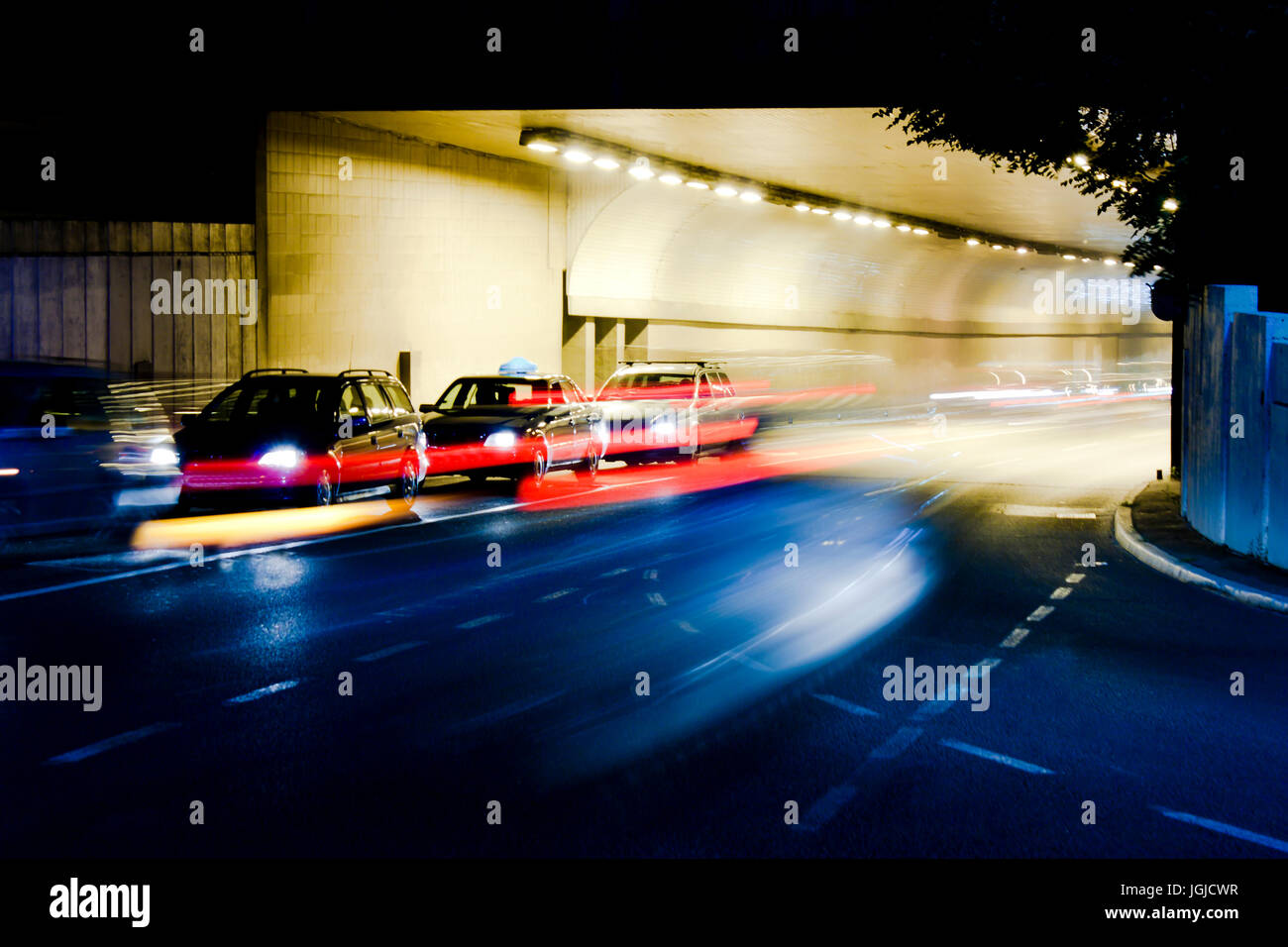 Night traffic on city streets.Cars at tunnel exit waiting at intersection while driving vehicles entering tunnel leaving colored light trails Stock Photo