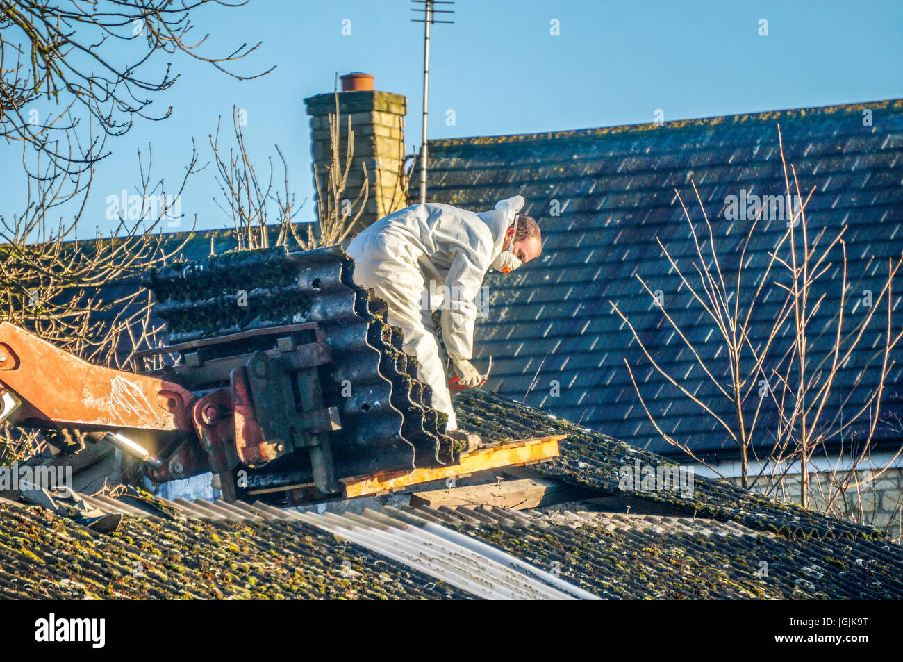 A man wearing protective clothing while removing asbestos roofing from