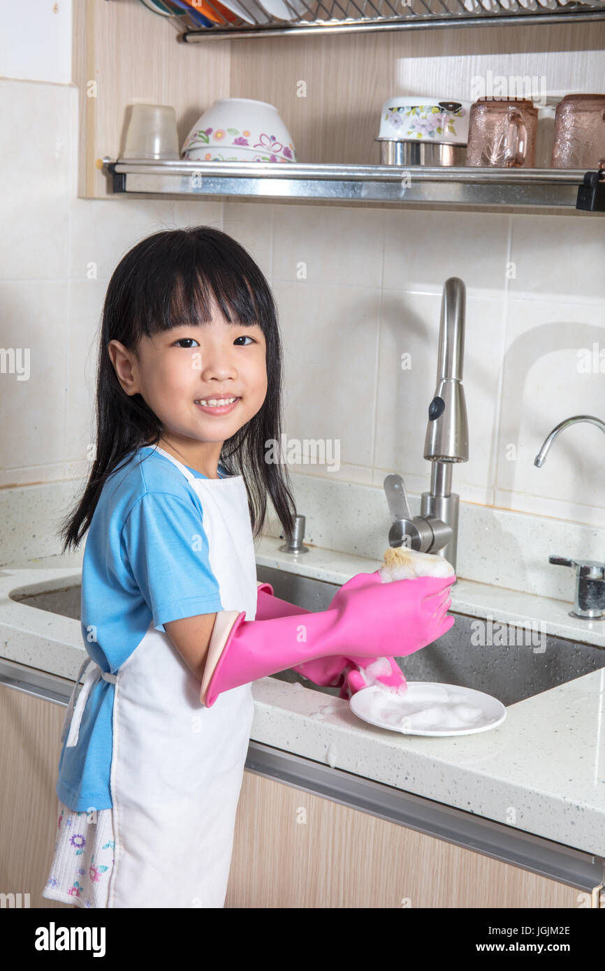 Asian Chinese little girl washing dishes in the kitchen at home Stock