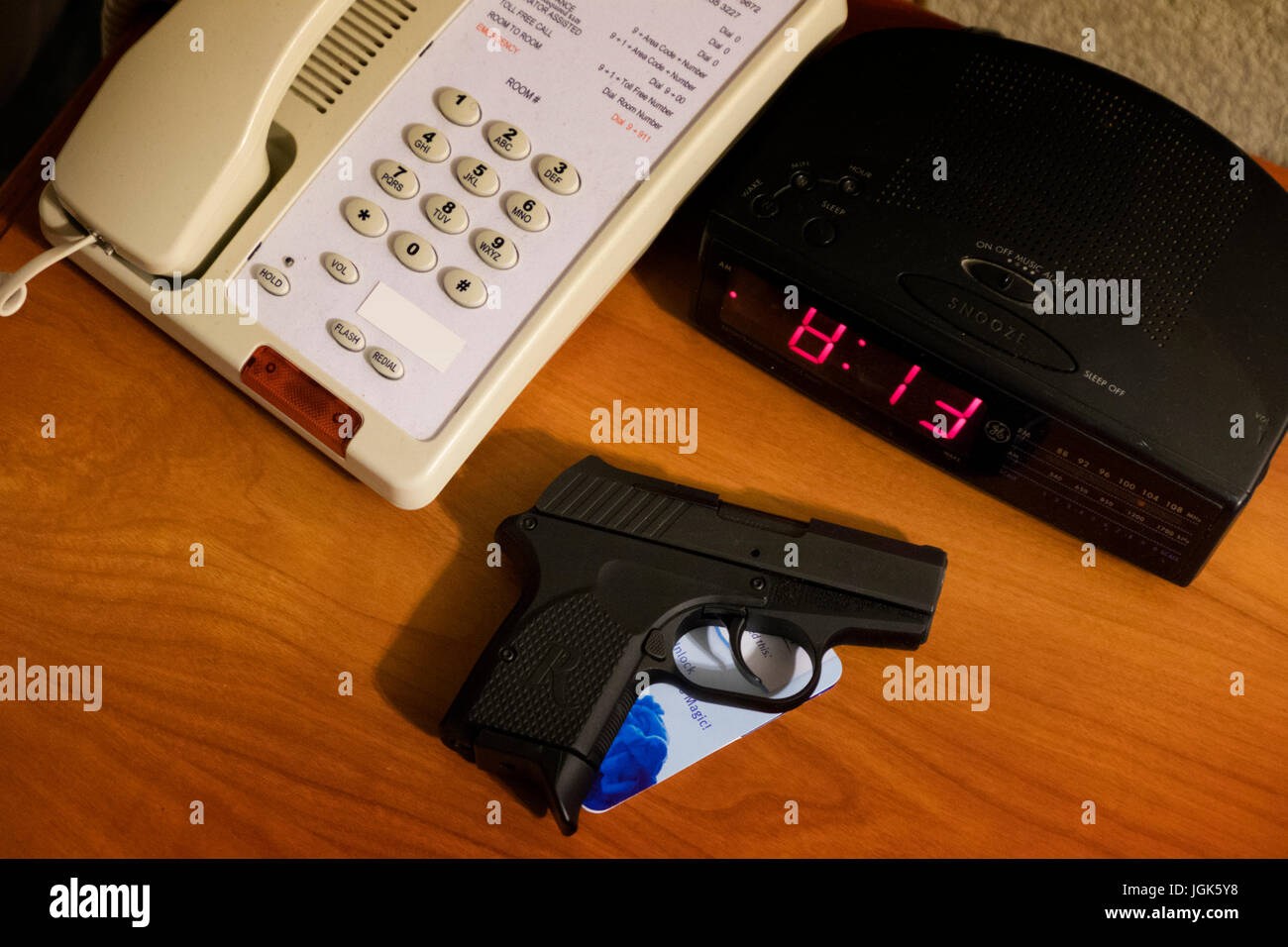 Handgun on a motel room bedside table with telephone and clock radio Stock Photo