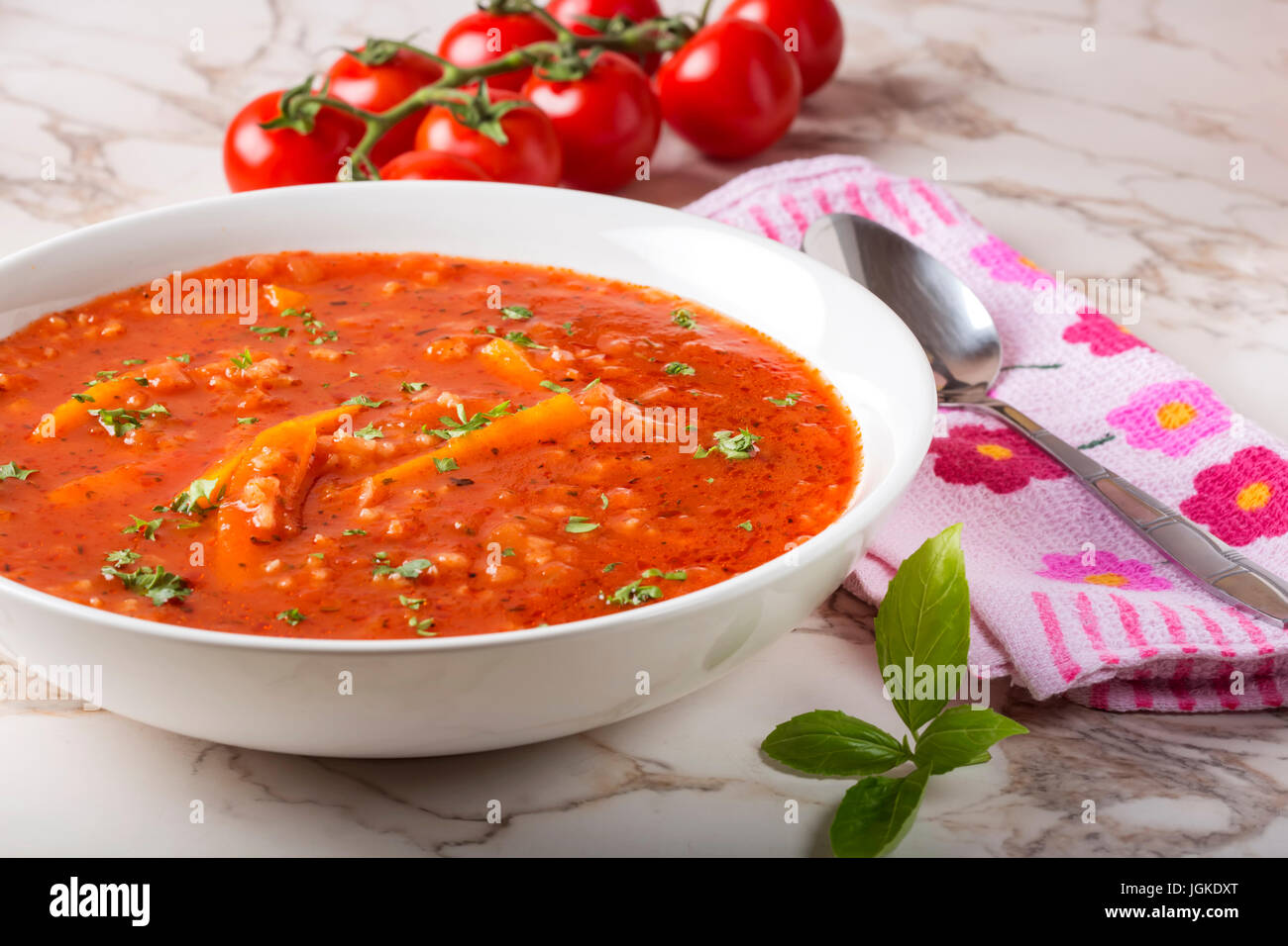 Summer soup made from tomato sauce, rice and carrot in white plate with spoon on towel Stock Photo