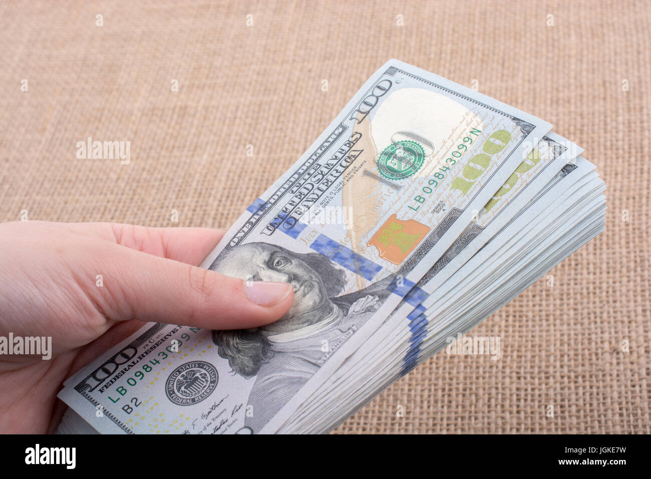 Hand holding banknote bundle of US dollar on a linen canvas background ...