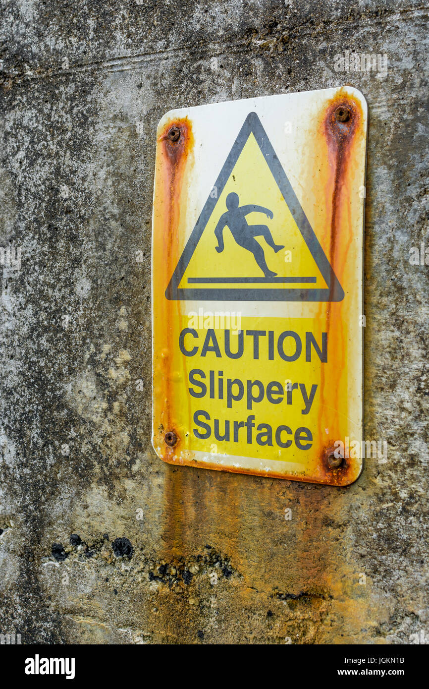 Yellow hazard warning sign identifying slippery surface present. Slippery slope metaphor. Public warning sign, falling man pictogram. Stock Photo