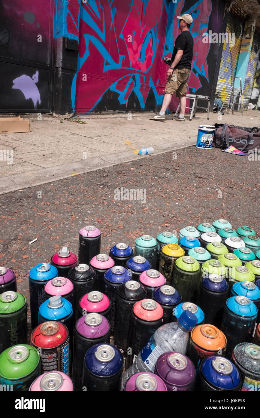 Graffiti artist painting a mural on a wall with spray cans in the ...