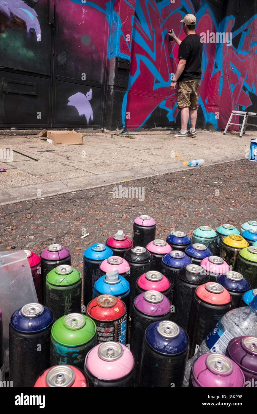 Graffiti artist painting a mural on a wall with spray cans in the ...