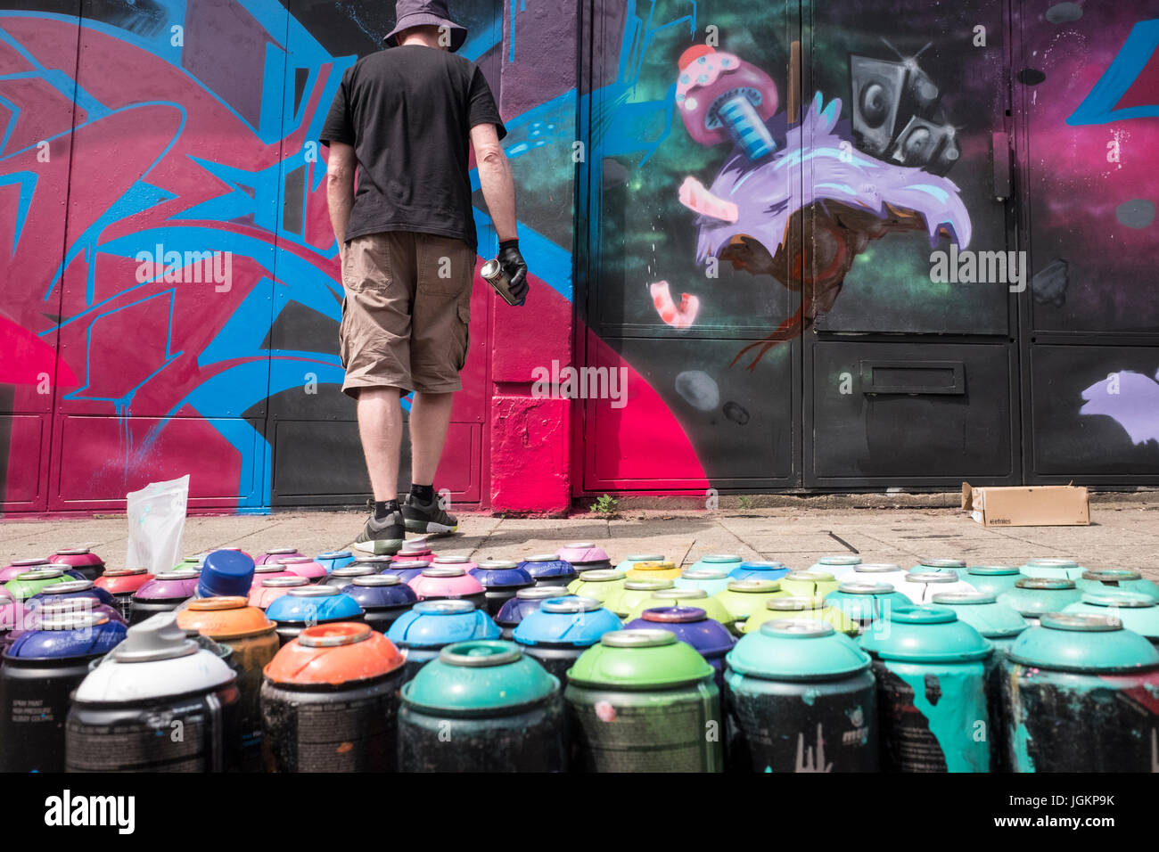 Graffiti artist painting a mural on a wall with spray cans in the ...