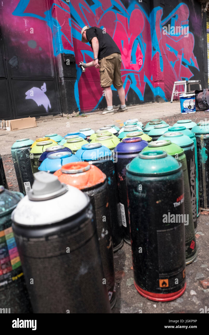 Graffiti artist painting a mural on a wall with spray cans in the ...