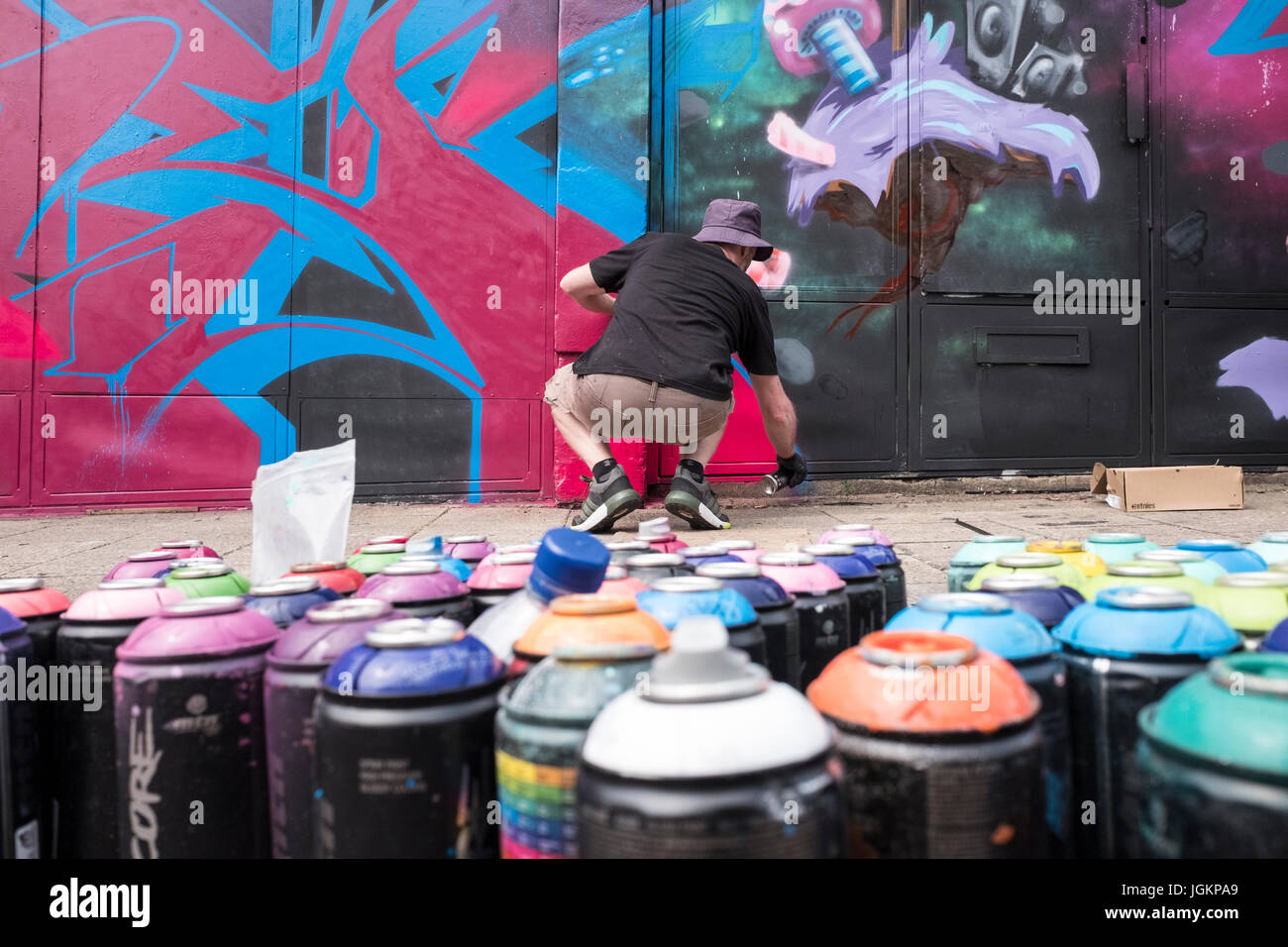 Graffiti artist painting a mural on a wall with spray cans in the ...