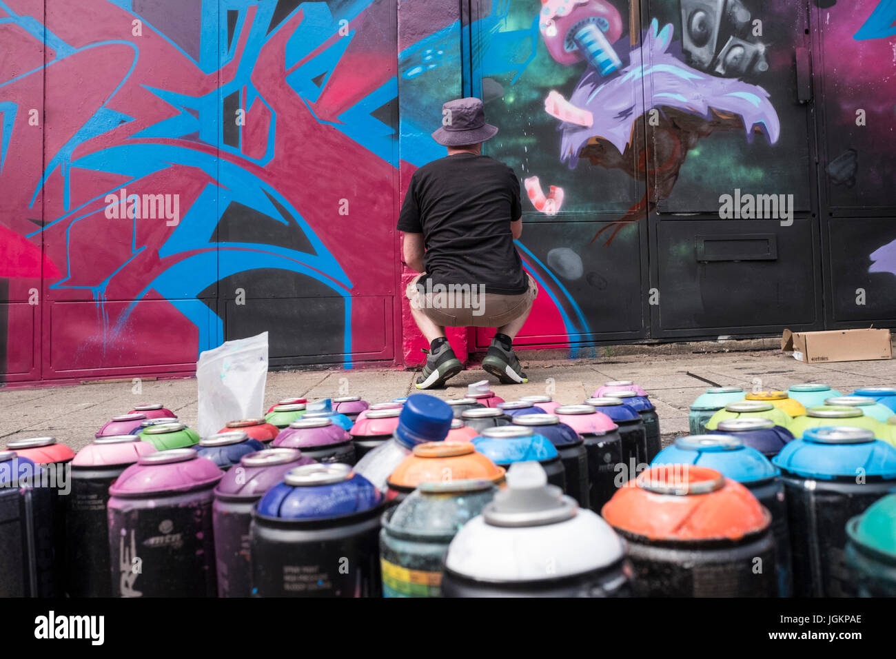 Graffiti artist painting a mural on a wall with spray cans in the ...