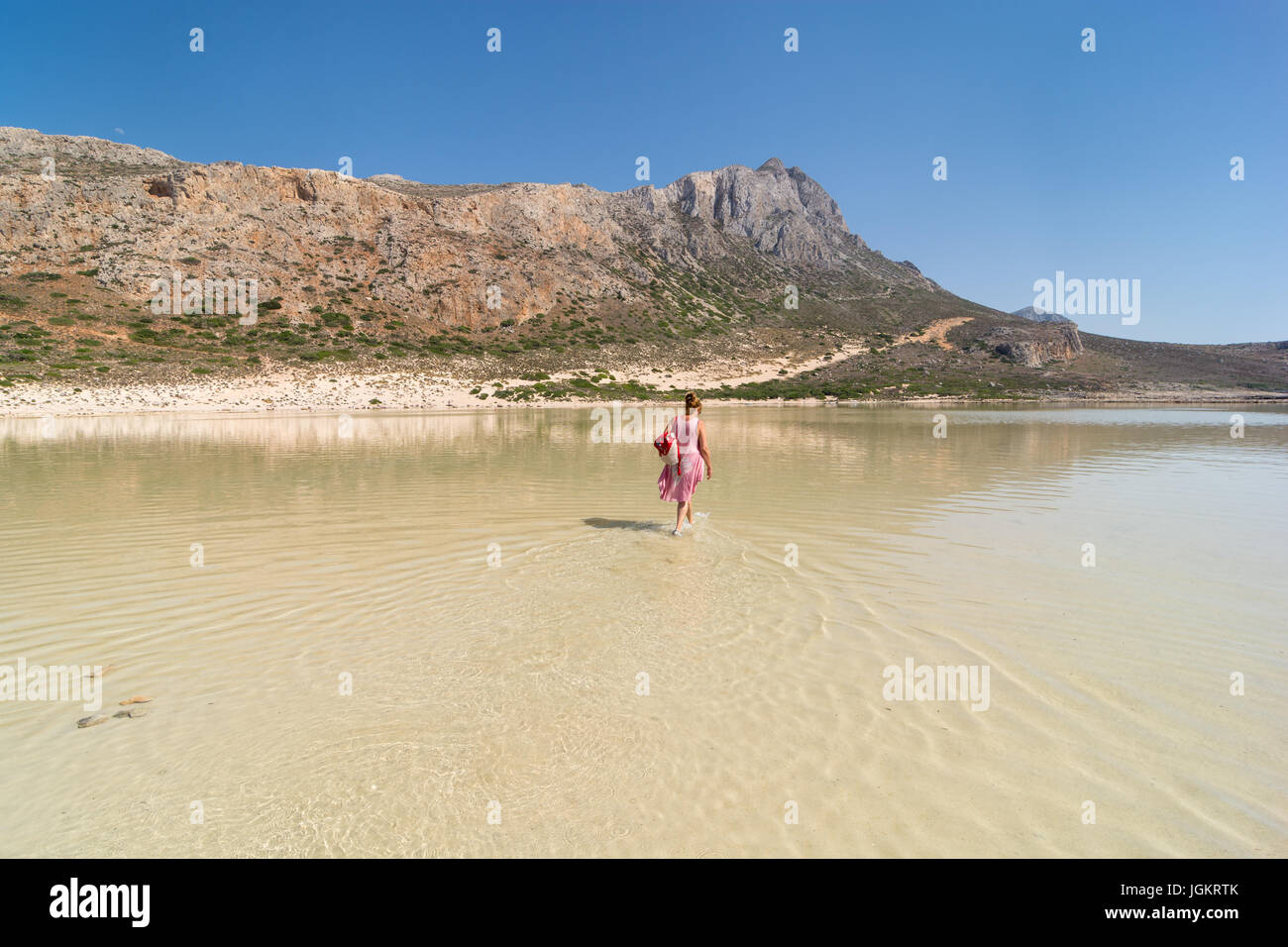A woman walking through the warm waters of the lagoon at Balos Beach, north-west Crete, Greece, on the western side of the Gramvoussa peninsula. Stock Photo