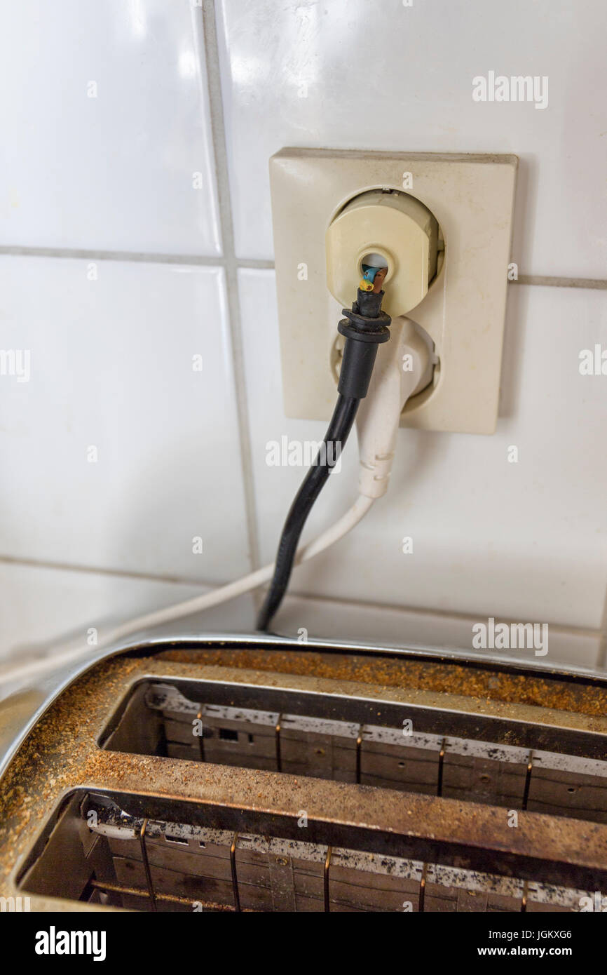 Worn out and dangerous electricity cable exposed going into wall socket above a toaster household appliance  Model Release: No.  Property Release: No. Stock Photo