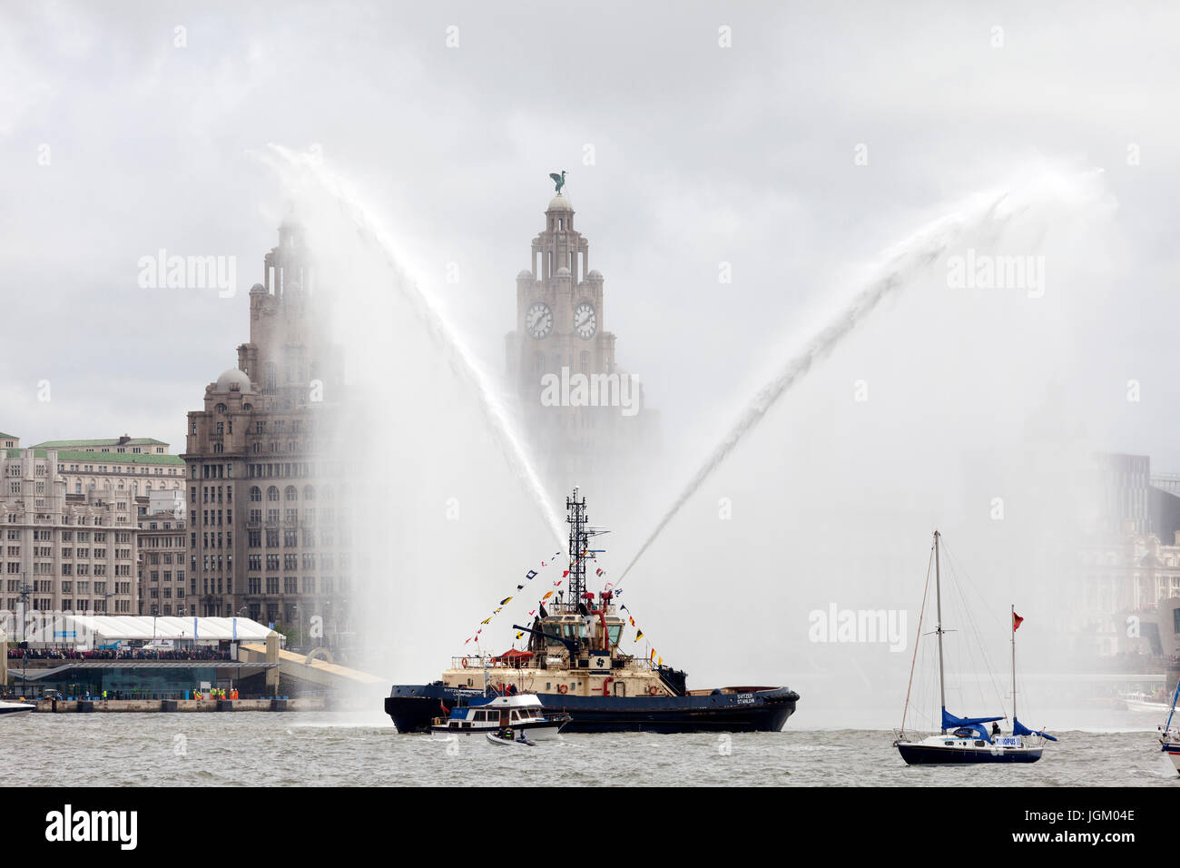 The tugboat Svitzer Stanlow sprays water in the River Mersey in front of the Royal Liver Building, Pier Head, Liverpool Stock Photo