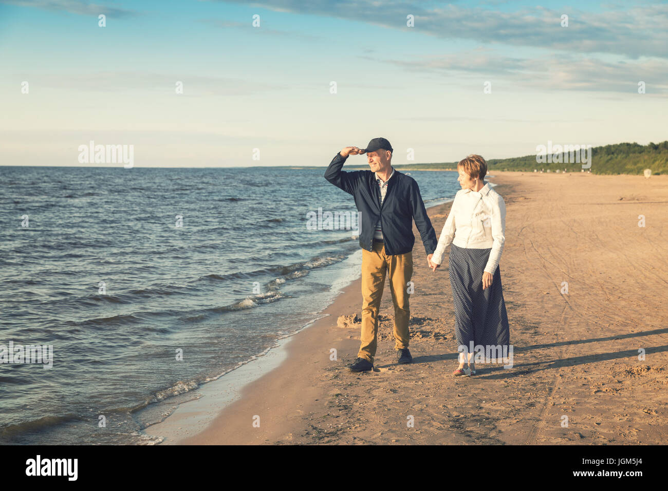 elderly couple having romantic walk on the beach at sunset Stock Photo