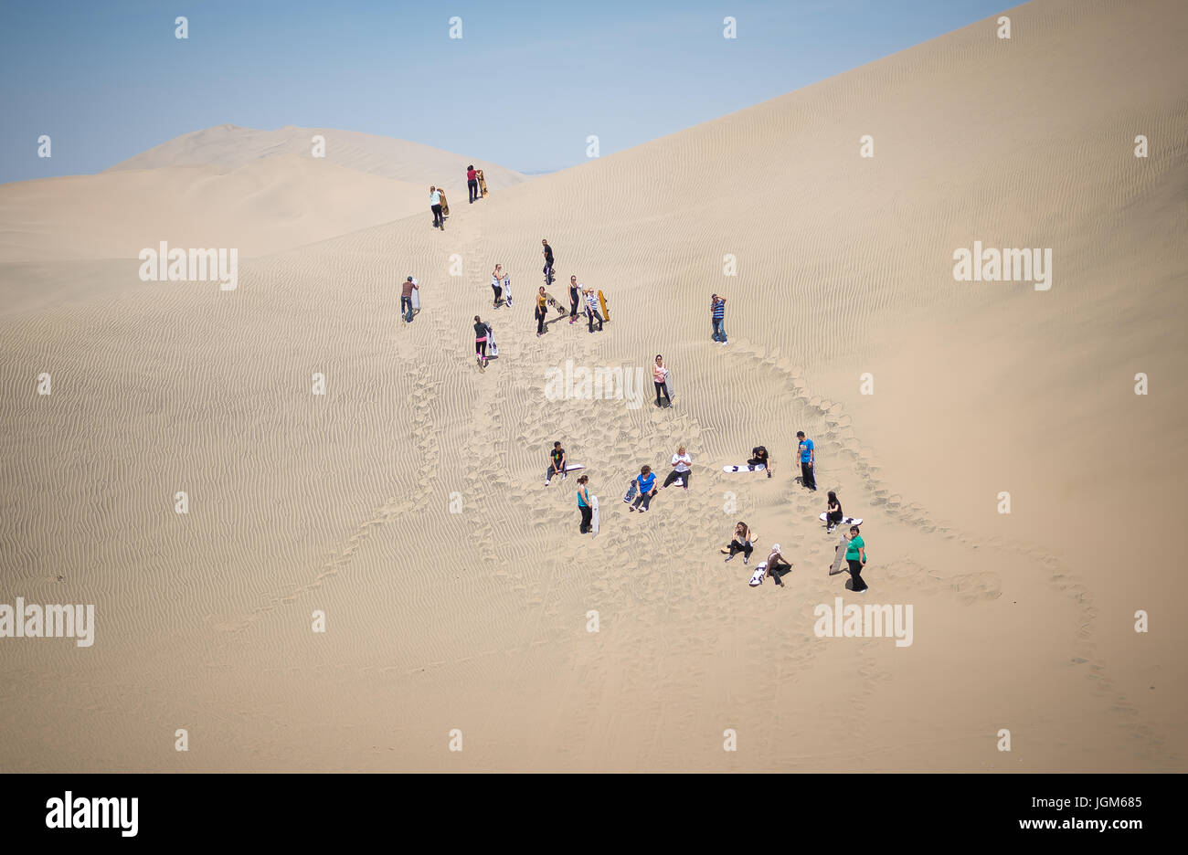 Far away shot of a group of tourists climbing up a sand dune to go sandboarding Stock Photo