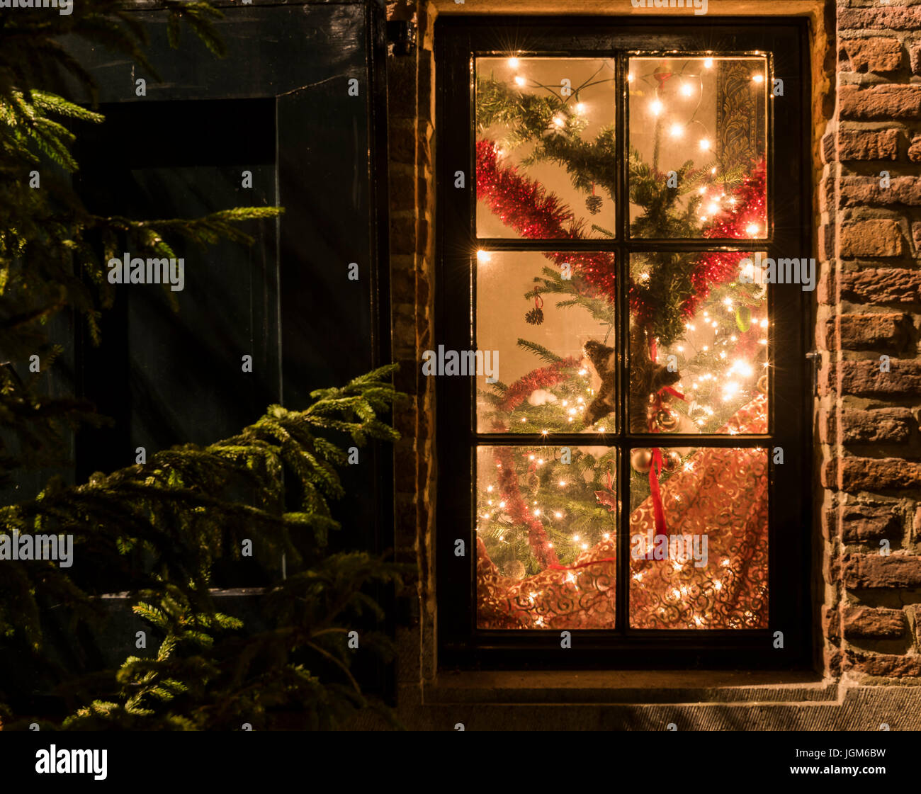 Christmas window with Christmas tree, lights, red garlands and Christmas star. Stock Photo