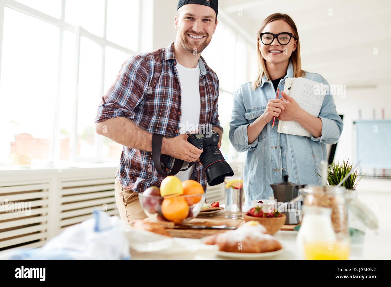 Young photographer and stylist standing by table with food Stock Photo