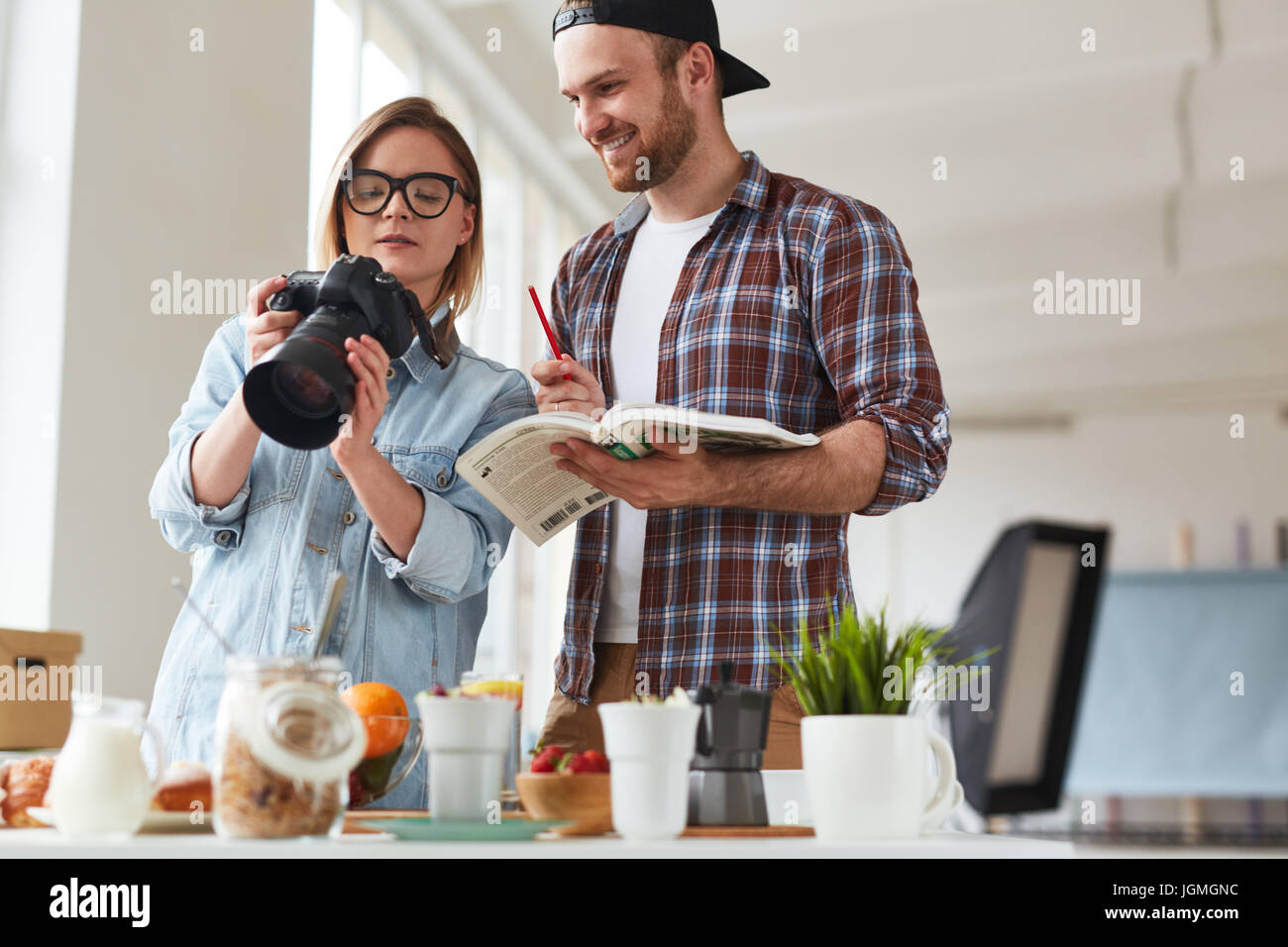 Young woman showing good shots in photocamera to colleague while shooting food Stock Photo