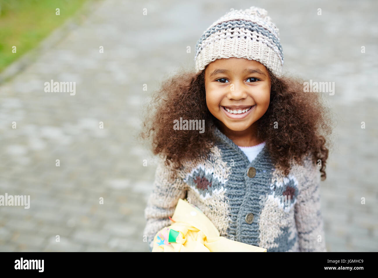 Portrait of cute African-American girl looking up at camera and smiling wearing knit hat and sweater on warm autumn day Stock Photo