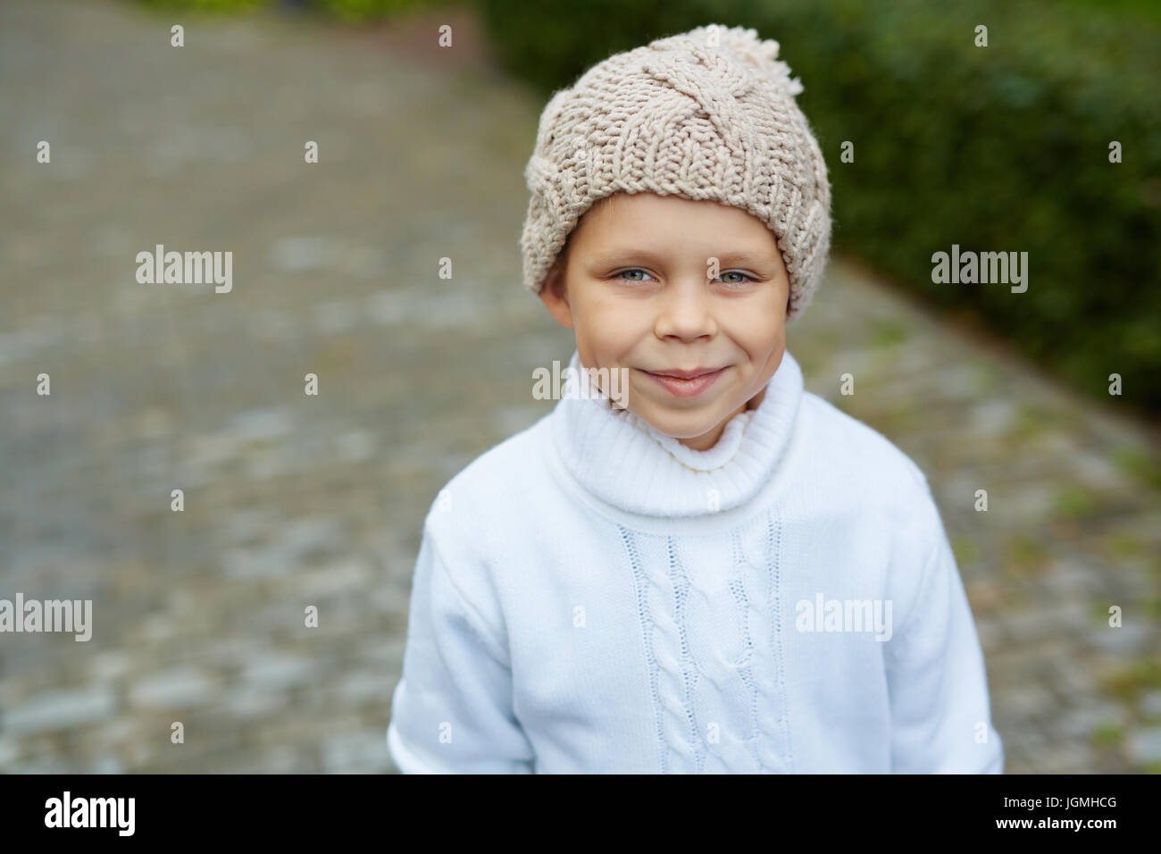 Portrait of cute blue eyed little boy wearing knit hat and sweater posing looking at camera on warm autumn day Stock Photo