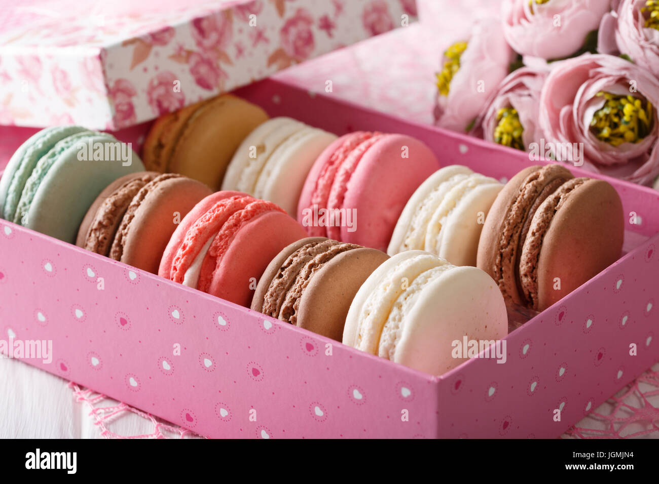 French macaroons in a pink box and flowers close-up on a table. horizontal Stock Photo