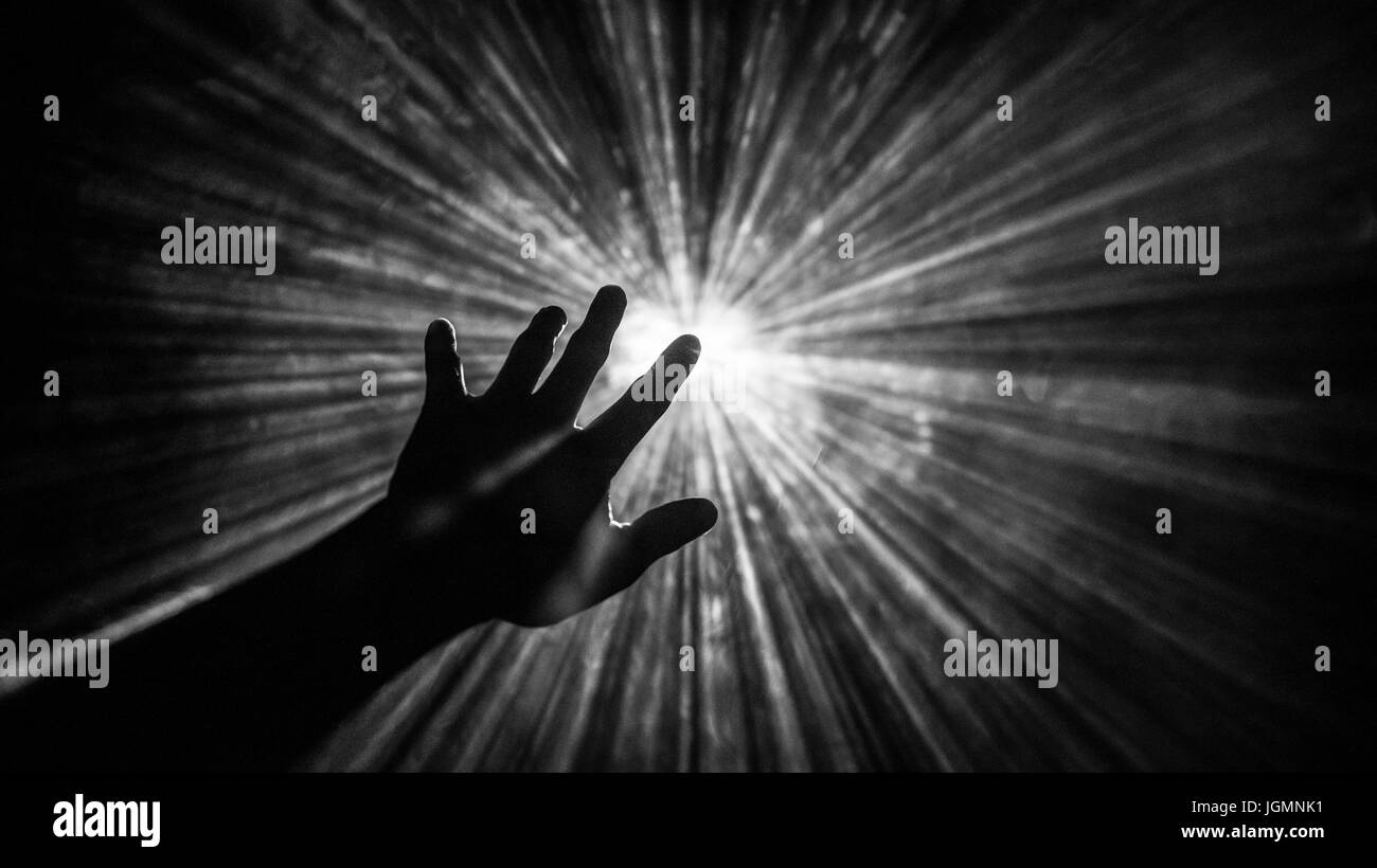 Hand reaches out to touch the light Stock Photo
