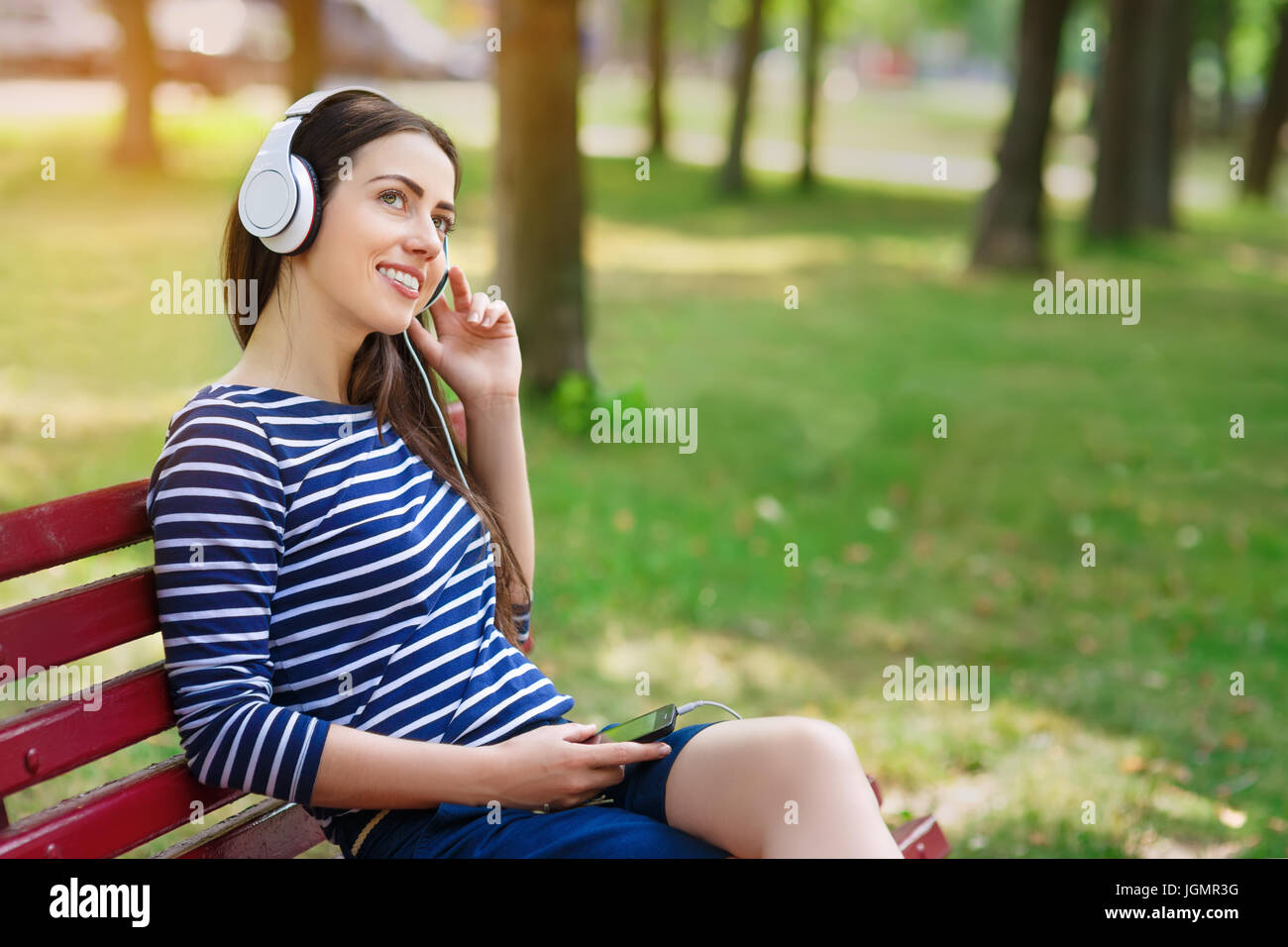 Young happy smiling brunette woman with headphones outdoors on summer day. Girl listening music in headphones in park Stock Photo