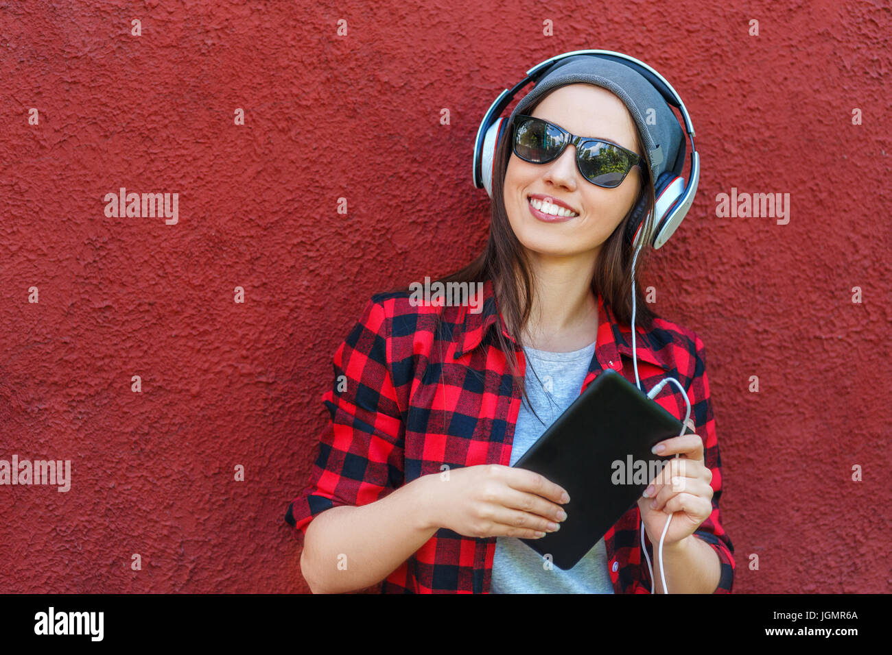 Portrait of happy hipster woman holding tablet computer and listening music in headphones. Girl using digital tablet outdoors. Copy space. Technology, Stock Photo