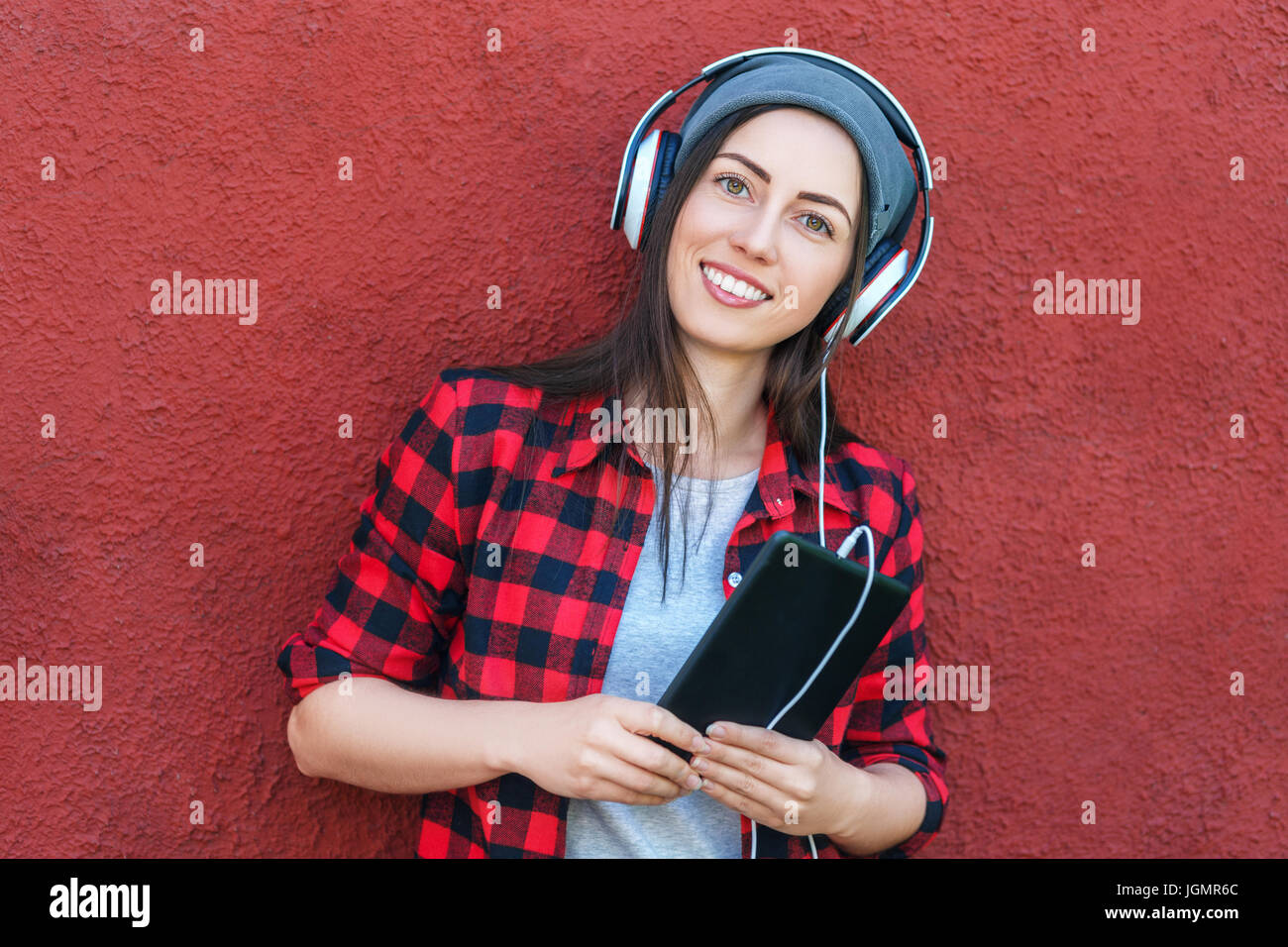 young woman holding tablet computer and listening music in headphones. Girl using digital tablet outdoors. Copy space. Technology, music, lifestyle, a Stock Photo