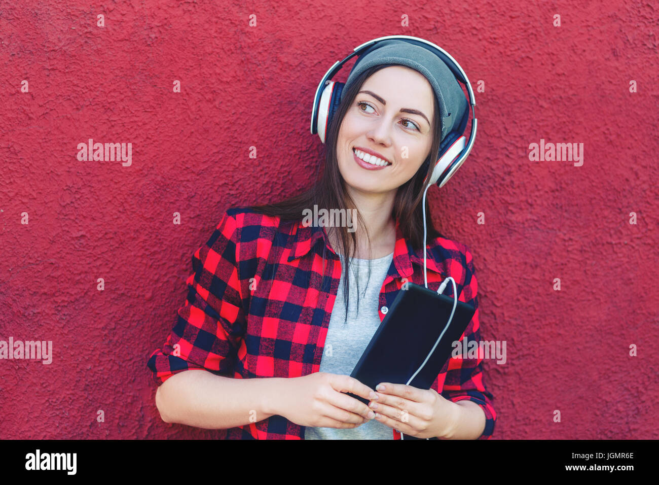 Portrait of happy hipster woman holding tablet computer and listening music in headphones. Girl using digital tablet outdoors. Copy space. Technology, Stock Photo
