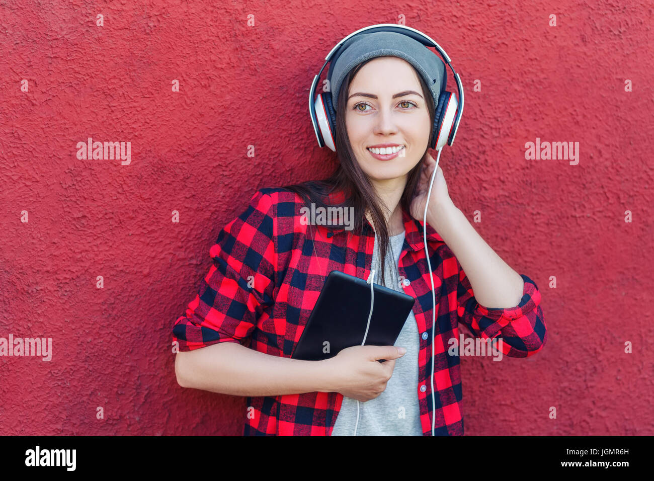 Portrait of happy hipster woman holding tablet computer and listening music in headphones. Girl using digital tablet outdoors. Technology, music, life Stock Photo