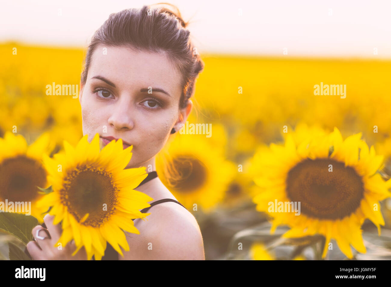 Beautiful natural young woman at sunflower field in summer sunset Stock Photo