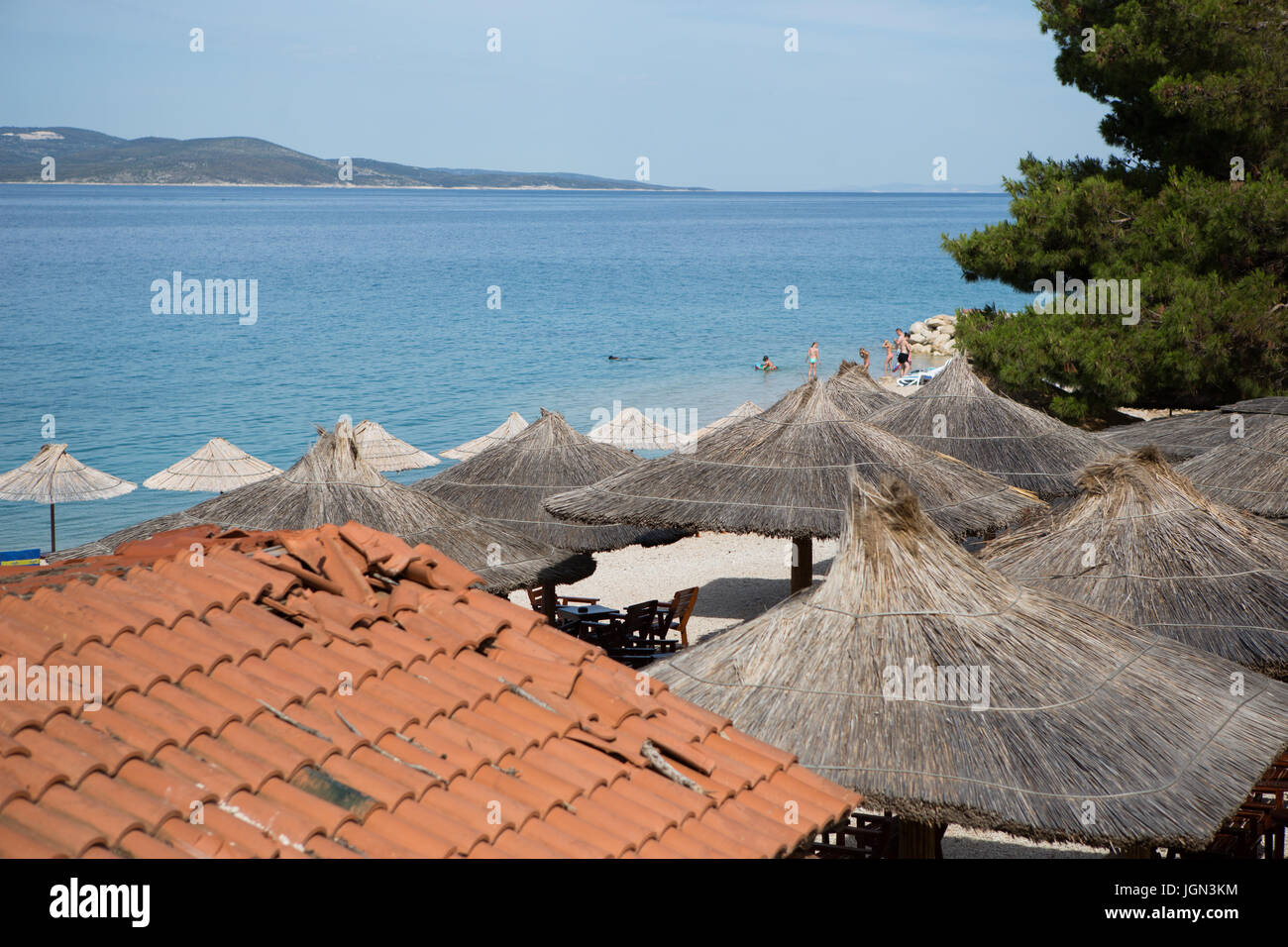 MAKARSKA,CROTIA - 16 JUNE,2017: Summer restaurant on the beach decorated with sun umbrella made from palm tree leaves.Beautiful landscape with deep bl Stock Photo