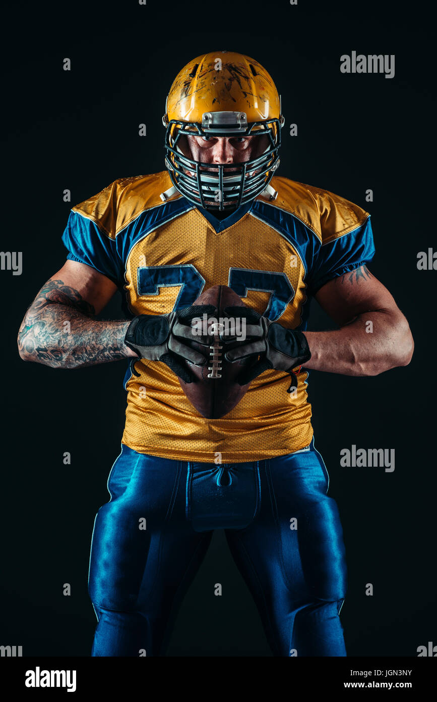 Muscular american football player in uniform and helmet holds ball in